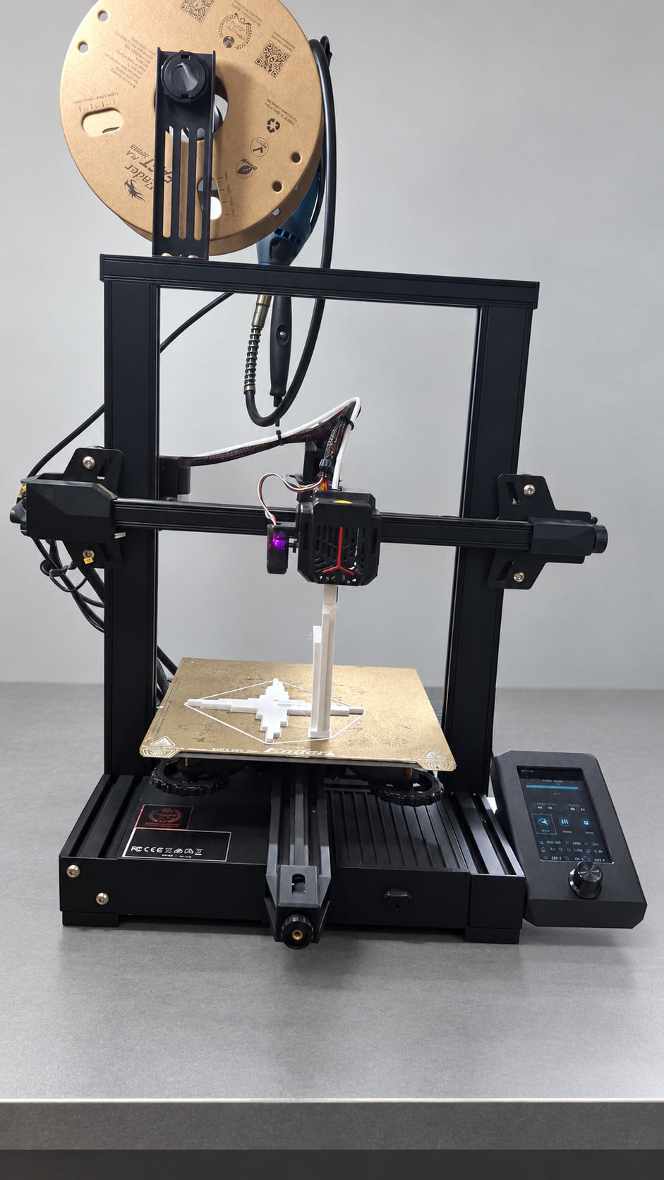 Creality Ender-3 V2 Neo com carretel de papelão e duas peças brancas de teste na mesa